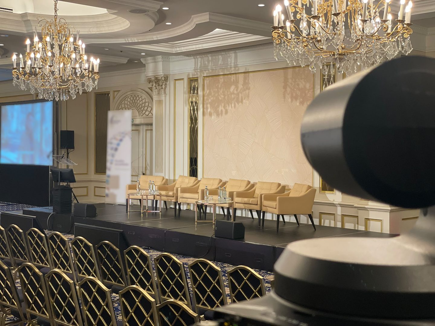 Salle de conférence prête pour le direct : plateau de table ronde, écran de projection et caméra au premier plan